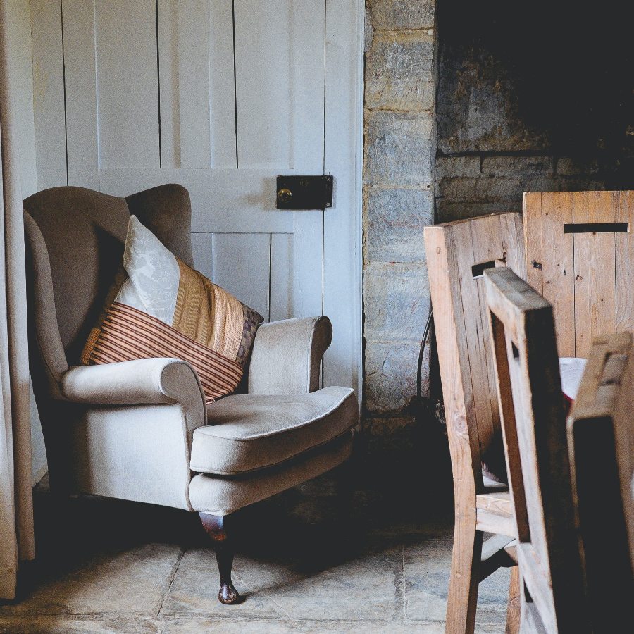 farmhouse setting with grey wing back armchair in front of a white door and next to rustic wooden dining chairs to the right