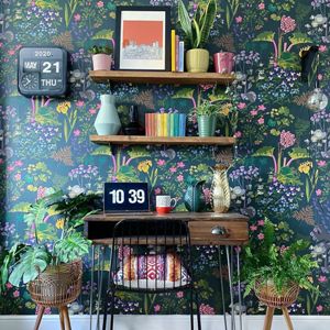 a home office location with desk and chair and shelves above and bright floral wallpaper in dark green blue