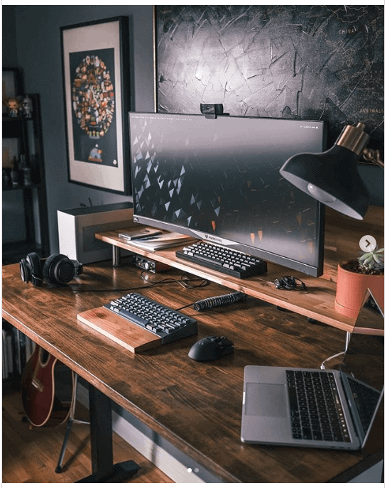 a home office desk setup in front of a dark wall as a background with large monitor and keyboard and laptop