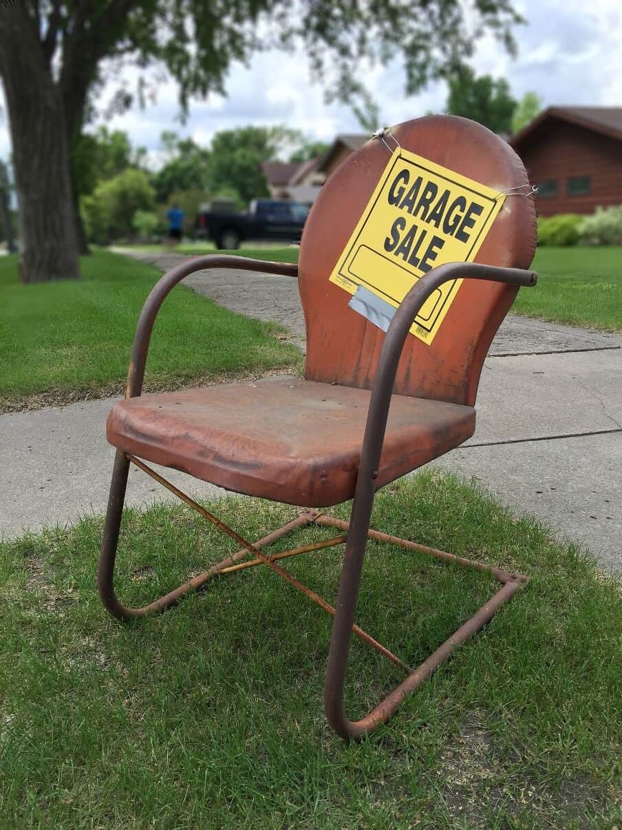 old metal framed chair with cushion with a garage sale sign hung on it 