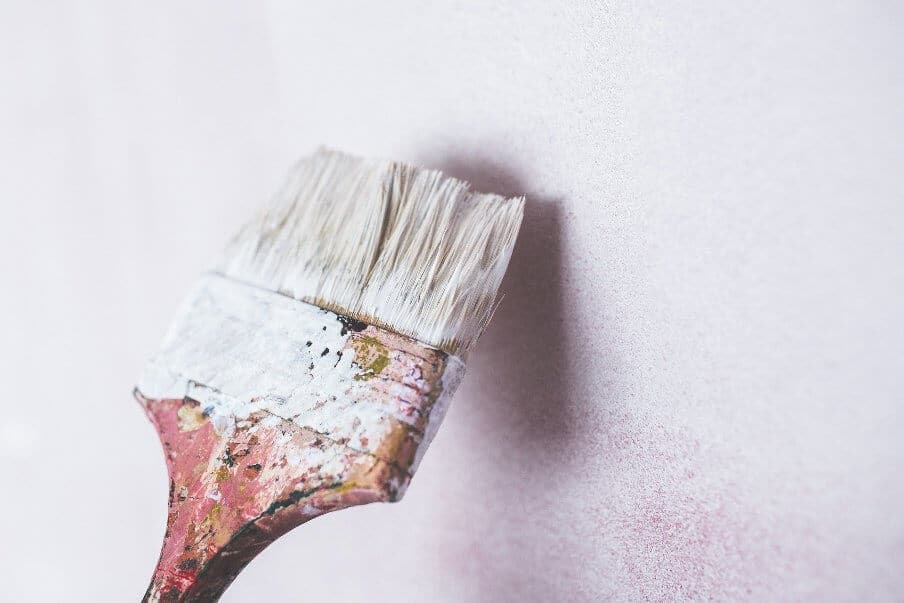 paint brush loaded with paint against a painted wall