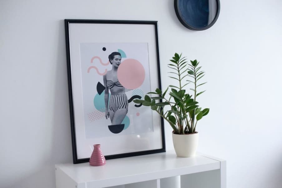 A colorful framed print sitting on a white unit and leaning against a white wall