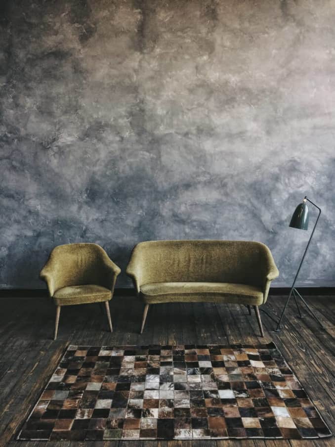an armchair and a two seater sofa in green velvet set against a dark floor and wall